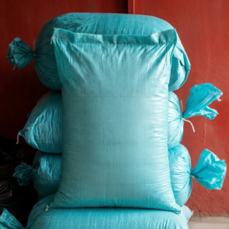 Stack of bright blue woven polypropylene feed sacks filled with snail feed calcium, displayed in front of a reddish-orange wall.