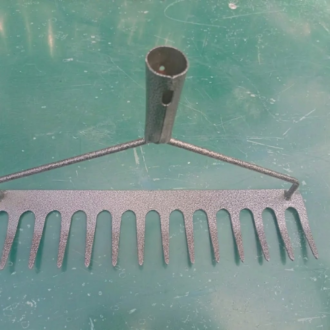 A heavy-duty metal rake head with sharp tines, positioned on a green surface