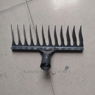 A black metal rake head attachment with curved tines, resting on a tiled floor."